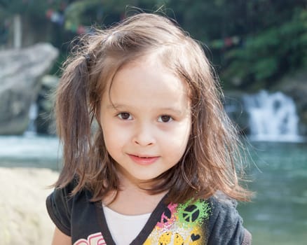 Child standing near a lake with waterfall in background