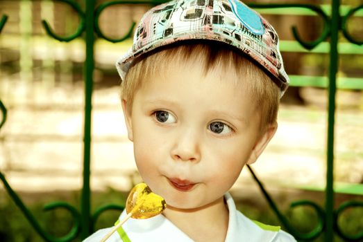 Little boy with lollipop in hand outdoors.