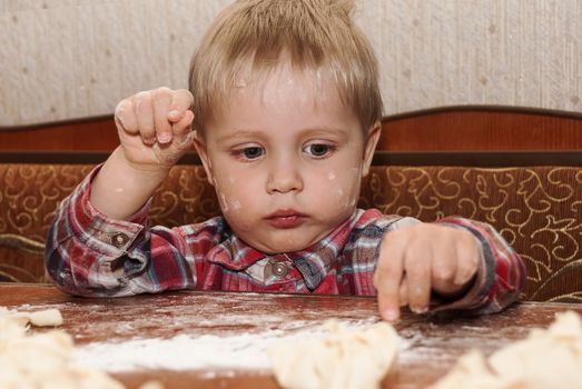 Little funny boy in the kitchen engaged in cooking