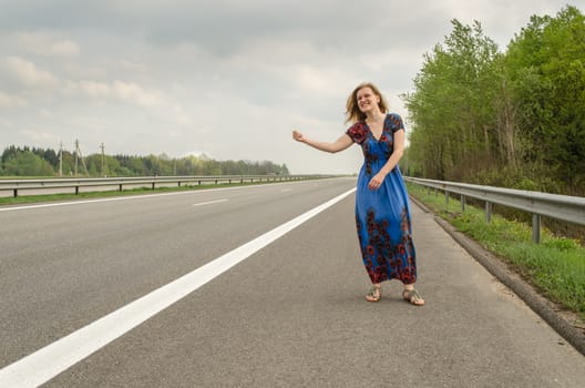 beautiful girl with long blue dress hitchhiking on the road