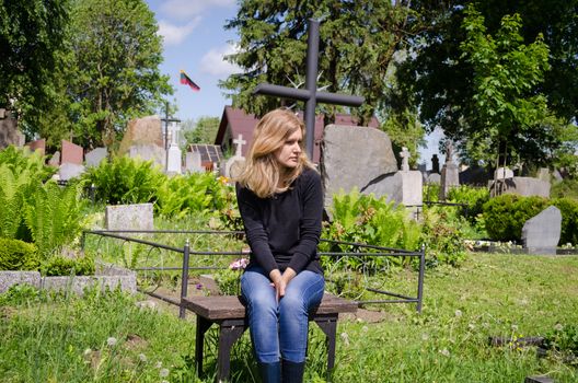 Sad woman sit near lover grave in cemetery. Patriot soldier died. National Lithuania flag.