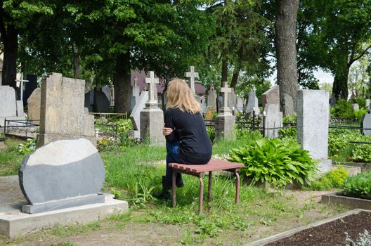 Sorrow woman shrinked near father husband tomb in cemetery.