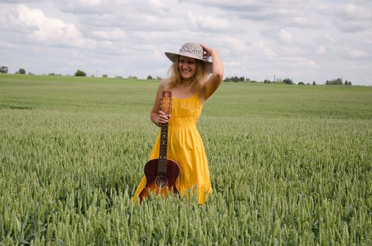 smiling young women with yellow summer dress and classical guitar pose in green wide rye field