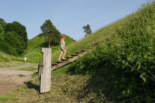 Young tourist girl climb on mound hills in Lithuanian historic capital Kernave, UNESCO World Heritage Site.