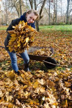 young woman hold large pile of dry autumn leaves in hands. Seasonal autumn garden work.