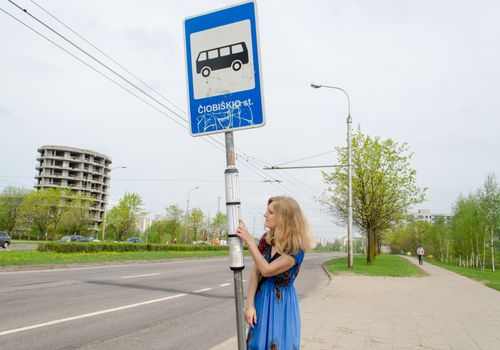 young blonde woman at the bus stop with bus pole tags driving schedules