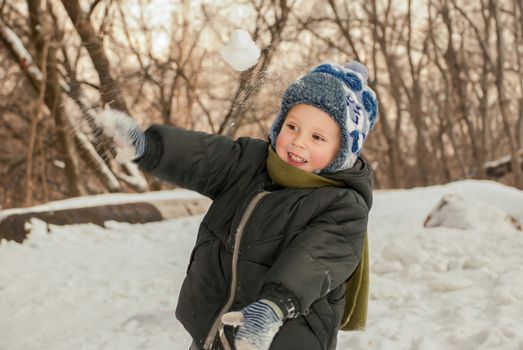Little boy playing in the snow outdoors in winter.