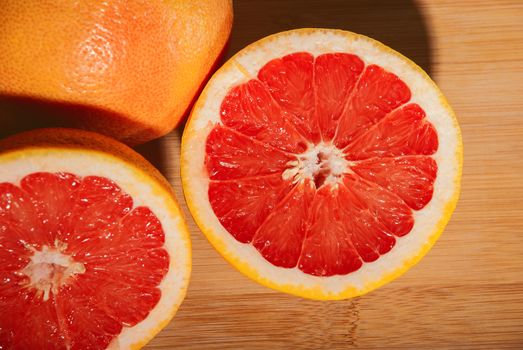 Slices of ripe red grapefruit on wooden board.