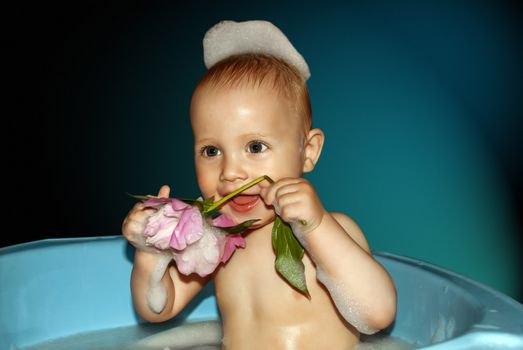 Little boy in bath with flower in hand on blue background.