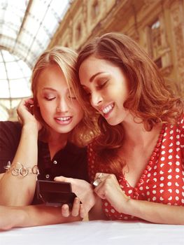 young women smiling and laughing as they look at text message on mobile phone 