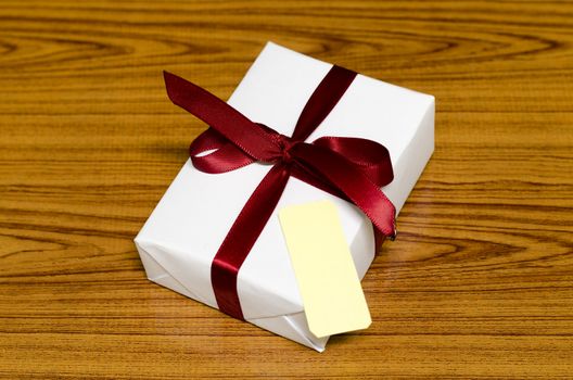 white gift box and red ribbin with tag on wood background