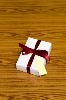 white gift box and red ribbin with tag on wood background