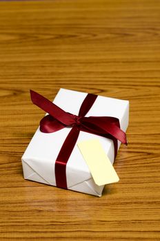 white gift box and red ribbin with tag on wood background