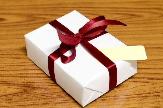 white gift box and red ribbin with tag on wood background