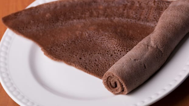 A Roll of Injera made from black teff on a white plate