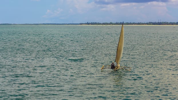A man sailing on a small handmade sailboat in the middle of the Indian Ocean