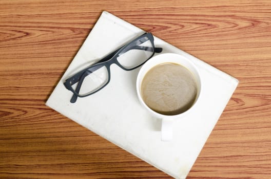 coffee cup and notebook with glasses on wood background