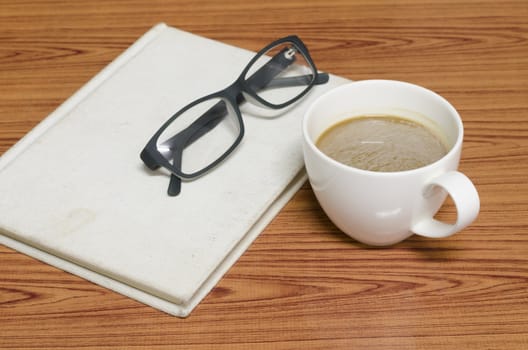 coffee cup and notebook with glasses on wood background