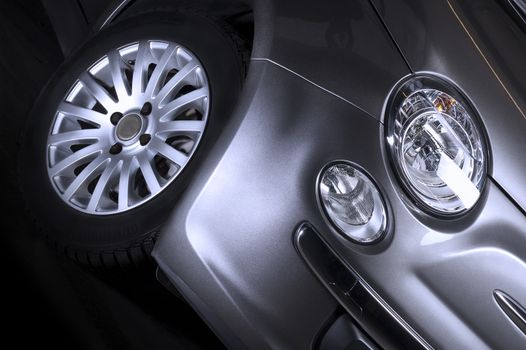 Detail of the front headlight , parking light and tyre of a silver car with a spoked alloy sports wheel , close up low angle