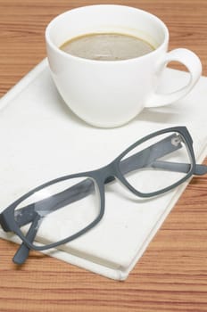 coffee cup and notebook with glasses on wood background