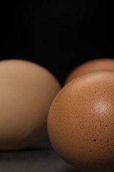 Closeup of farm fresh brown free range hens eggs showing the texture of the shell with shallow dof, vertical format on a dark background with copyspace