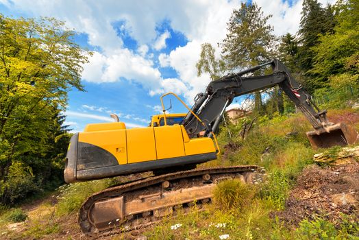 Tracked excavator yellow and black at woods and blue sky with clouds