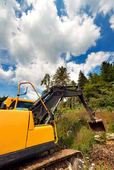 Close up of tracked excavator yellow and black at woods and blue sky with clouds