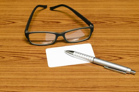 business card and pen with glasses on wood background