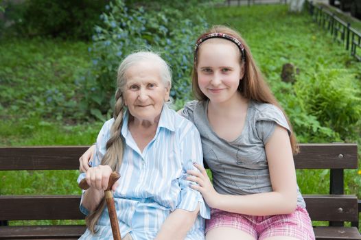 Granddaughter hugs grandmother sitting on a bench in the garden