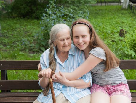 Granddaughter hugs grandmother sitting on a bench in the garden