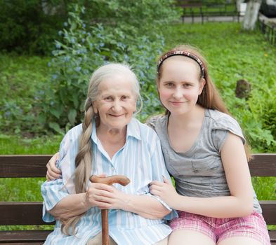 Granddaughter hugs grandmother sitting on a bench in the garden