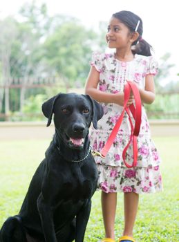 Cute Indian girl with her labrador retriever pet dog at outdoor park.