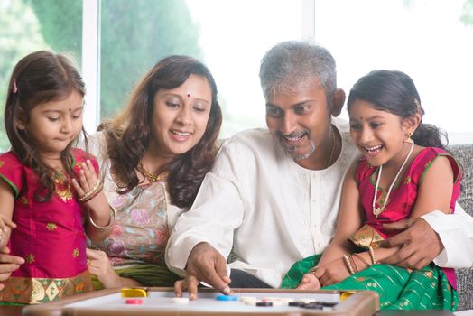 Happy Asian Indian family playing carrom game at home. Parents and children indoor lifestyle.