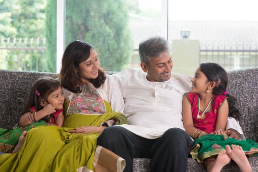Happy Indian family at home. Asian parents chit chatting with their kids, sitting on sofa. Parents and children indoor lifestyle.