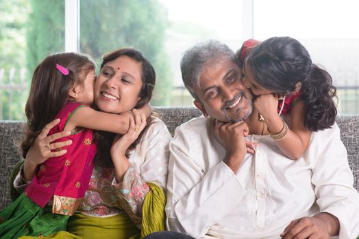 Happy Indian family at home. Asian girls kissing their parents, sitting on sofa. Parents and children indoor lifestyle.