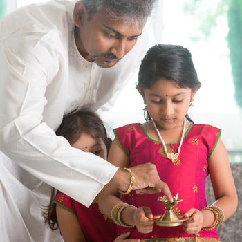 Indian family in traditional sari preparing to celebrate diwali or deepavali at home. Little girl hands holding oil lamp during festival of light.