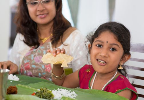 Indian family dining at home. Little girl eating snack papadum. India culture.