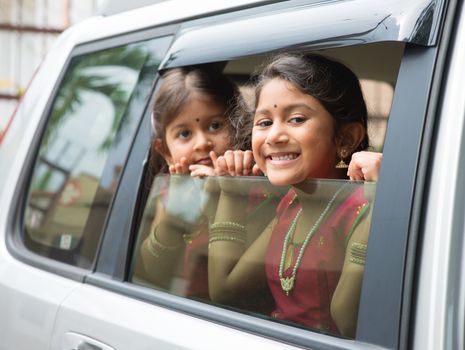 Asian Indian family going to a vacation. Happy children sitting inside car with window open looking out. 
