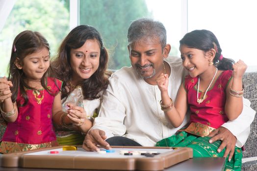 Asian Indian family playing carrom game at home. Parents and children indoor lifestyle.