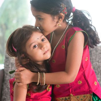 Indian girl kissing her younger sister with love. Asian family at home. Beautiful daughters in traditional India sari.