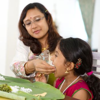 Indian family dining at home. Candid photo of Asian mother feeding rice to child with hand. India culture.