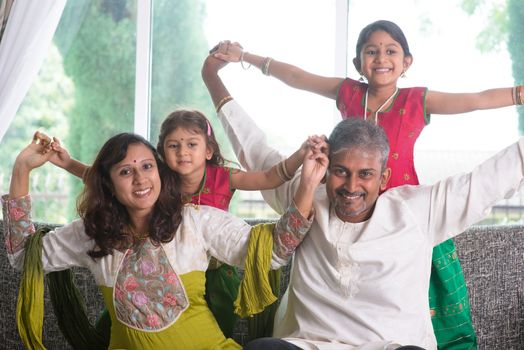 Happy Indian family at home. Asian parents playing with their kids, sitting on sofa. Parents and children indoor lifestyle.