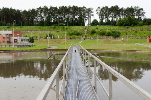 Sewage treatment mechanism spinning and filtering water in basin. Mew birds sit on railings.