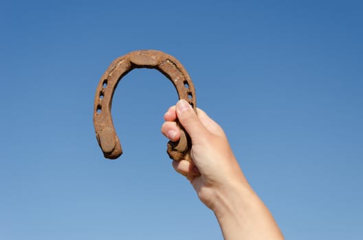 female hand hold vintage metallic rusty horseshoe on blue sky background