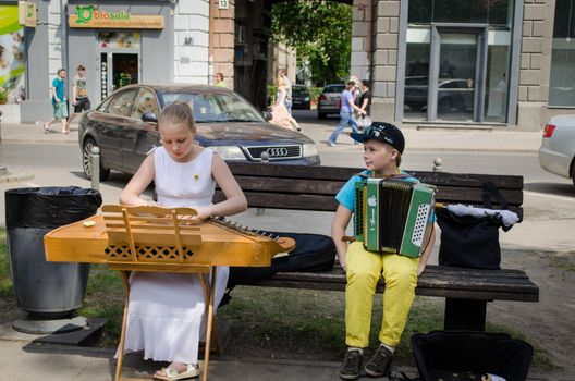 VILNIUS, LITHUANIA - MAY 18: young street music festival participants girl with baltic psaltery and boy with accordion on the bench on May 18, 2013 in Vilnius.