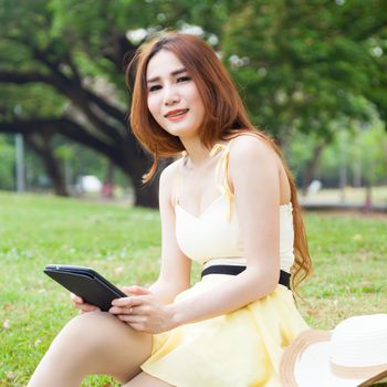 Woman sitting on lawn Hand holding tablet and thinking.