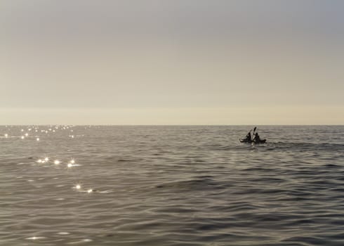Backlighting of a couple paddling with kayak at sunrise on a completely calm sea.