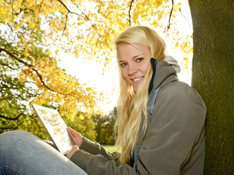 happy young blond woman with digital tablet in autumn park