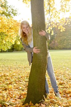  laughing young woman hugging a tree in autumn park