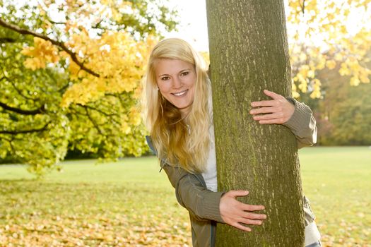 laughing young blond woman hugging a tree in autumn park